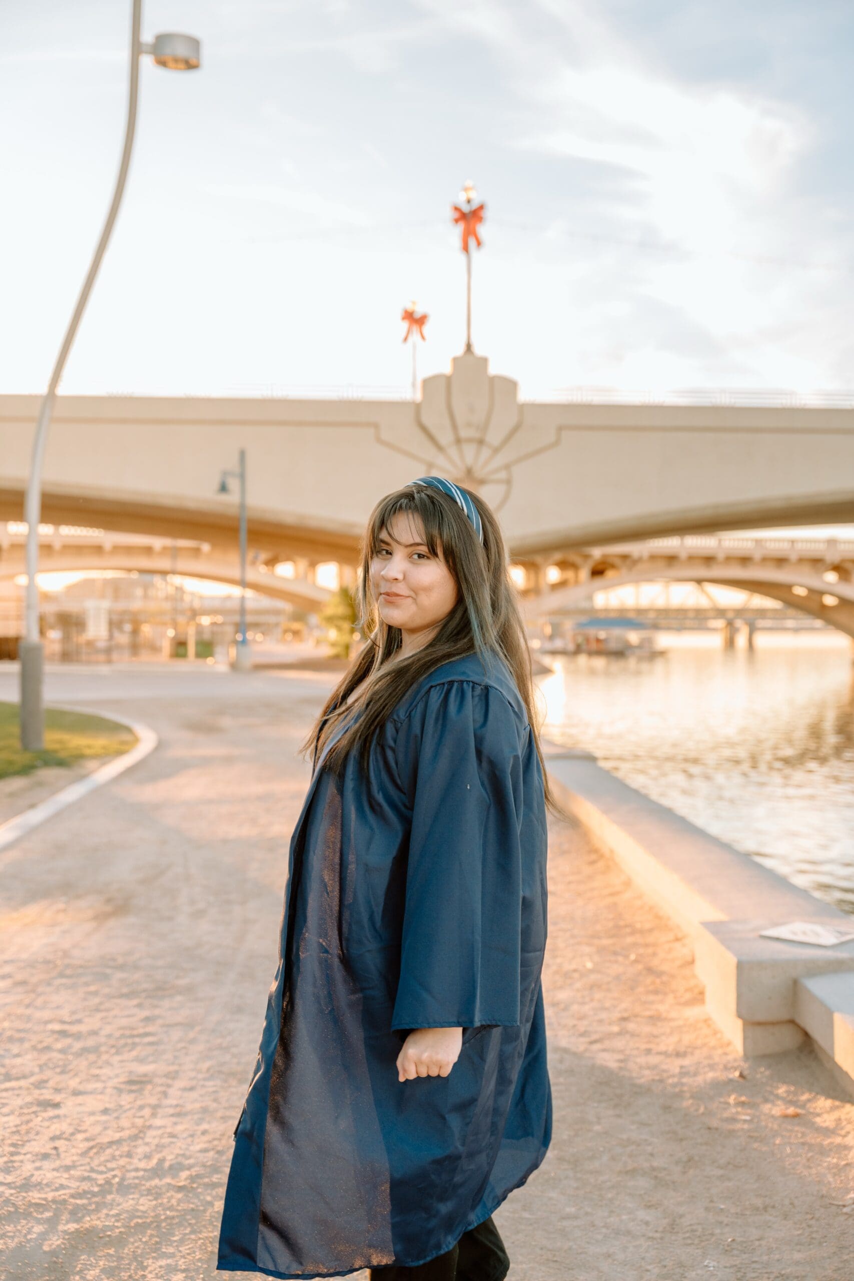 2026 High School Graduate walking down pathway nearby man-made river in city landscape.