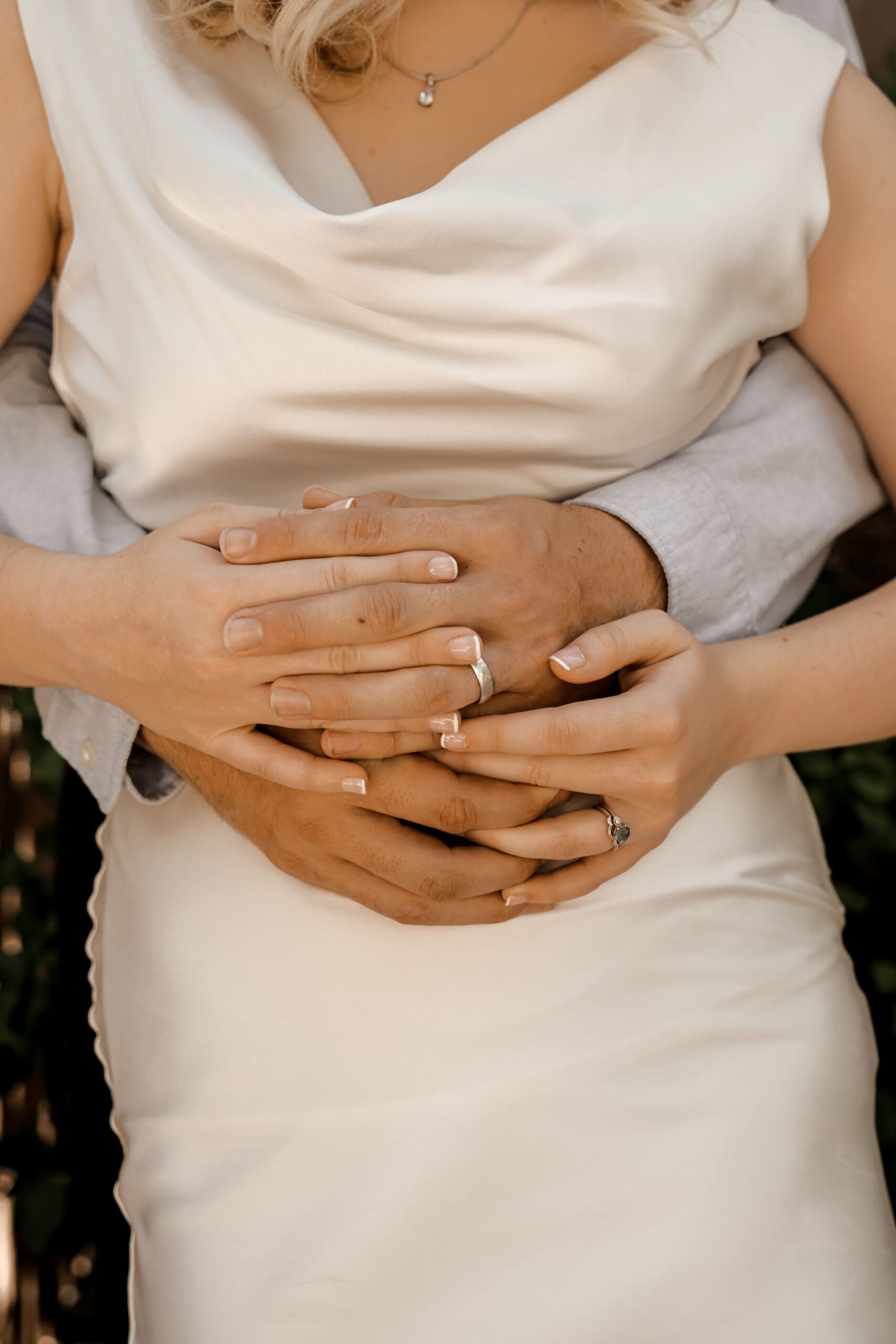Newly engaged couple holding caps showing off their new wedding bands. Hands held together at bride's waist.